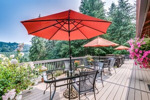 A wooden deck with outdoor furniture and red umbrellas, surrounded by lush greenery and flowers. - Misty Valley Inn B&B (Forks)