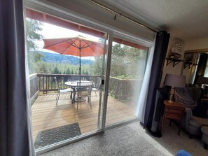 Puerta corrediza de vidrio que da a una terraza al aire libre con una mesa, sillas, una sombrilla y vistas a un área boscosa.