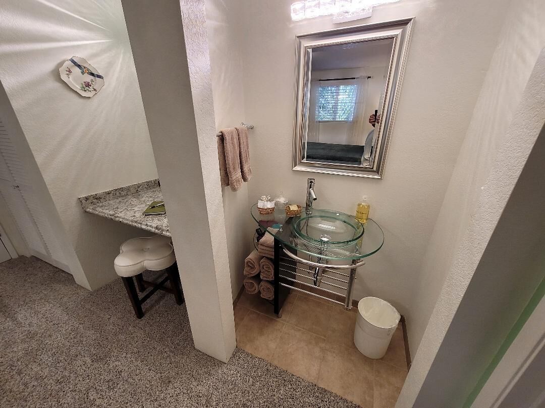 A bathroom with a glass sink, a mirror, a towel rack, and a toilet.