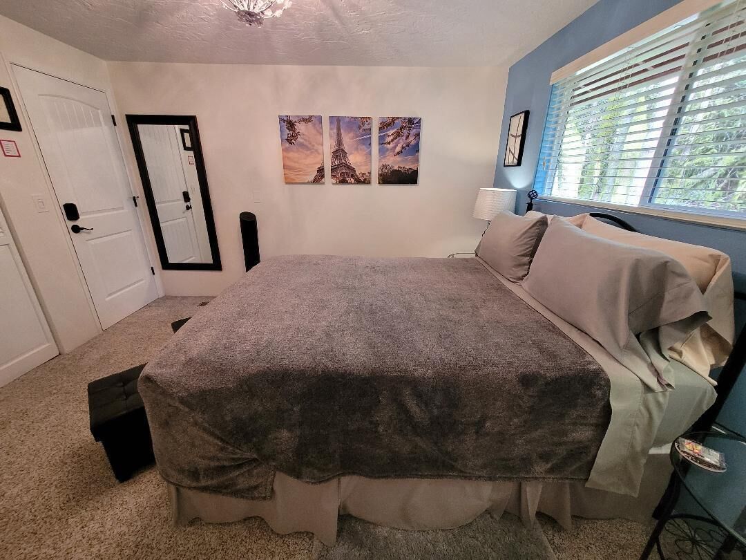 A bedroom with a bed, a nightstand, a lamp, and a window with blinds.