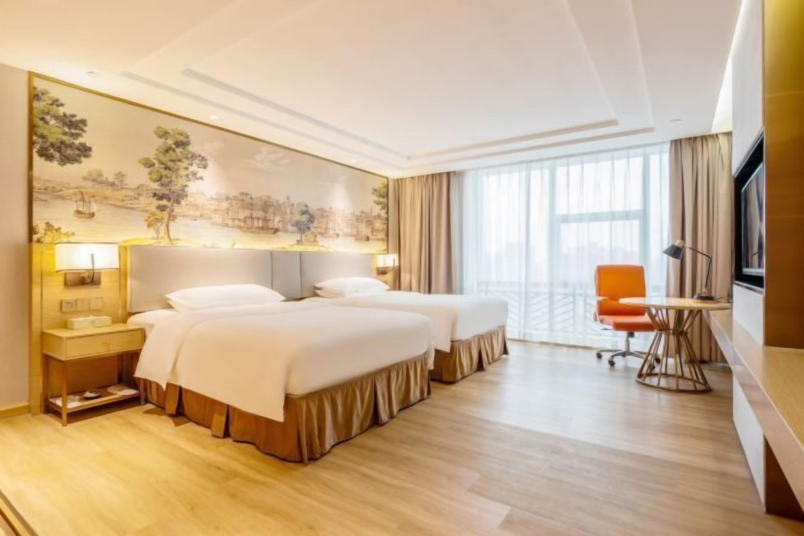 A hotel room with two beds, a desk, a chair, a TV, and a large window.