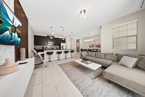 A modern living room with a sofa, coffee table, and a kitchen area in the background. - Poolside Bliss: Enchanted 4BR Townhome, Ultimate Fun! - 1556 (Davenport)
