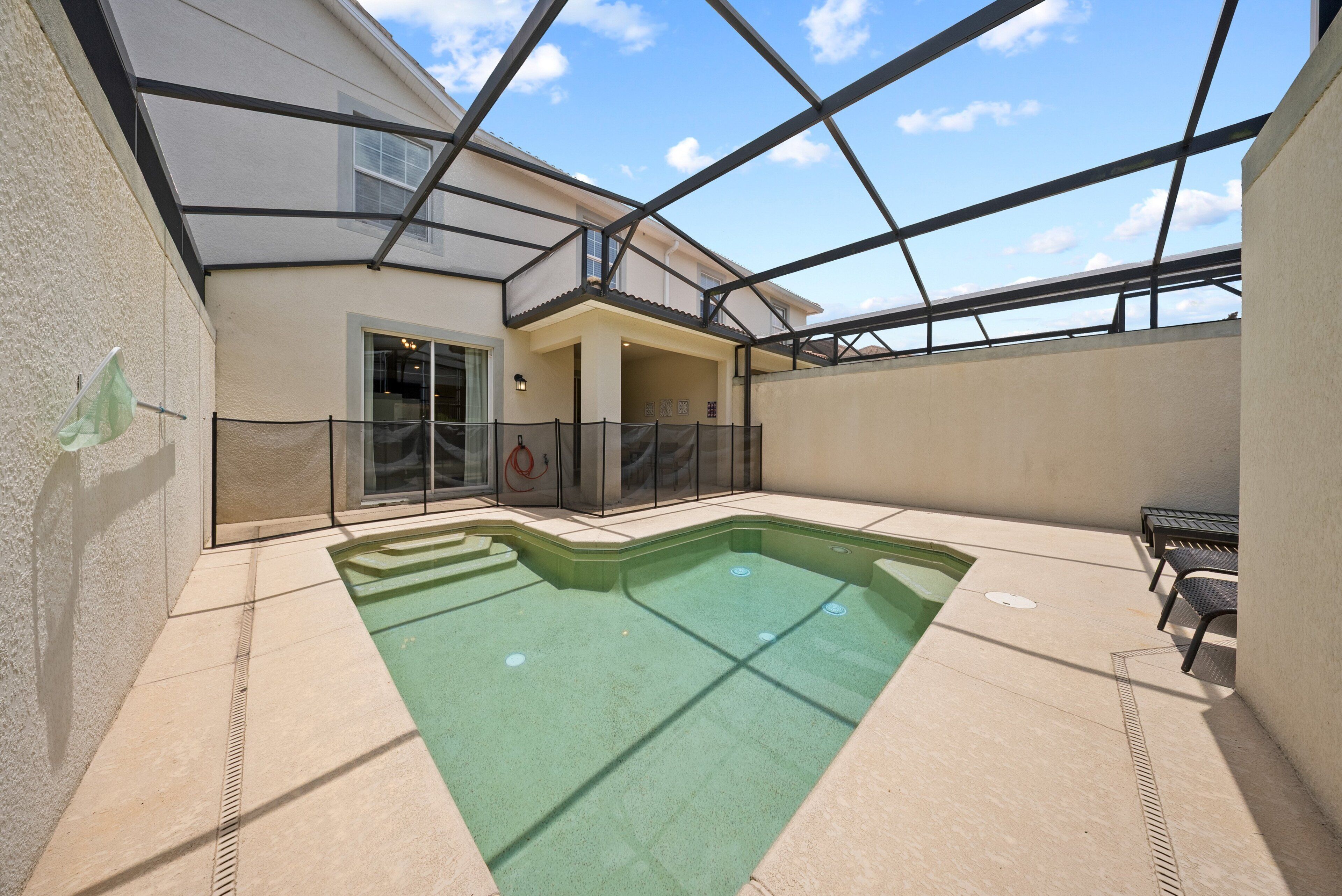 A swimming pool with steps leading into it, surrounded by a covered patio area with a glass ceiling.