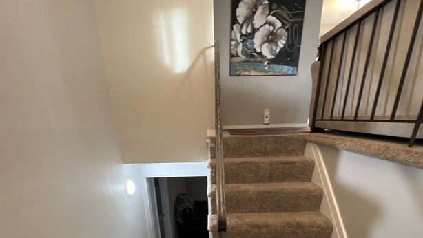 A carpeted staircase with a handrail, a wall-mounted light fixture, and a door leading to another room.