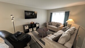 A living room with a black leather sofa, a beige sofa, a coffee table, a TV, a side table, and a lamp.