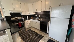 A modern kitchen with white cabinets, a black countertop, a stainless steel oven, a dishwasher, and a refrigerator.