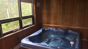 Eine Holzhütte mit einem Whirlpool in der Mitte, einem Fenster links und einer Holzwand.