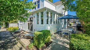 A white two-story house with a covered patio area, a small garden, and a wooden fence.
