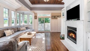 A spacious living room with a fireplace, a large TV, and a view of the outdoors.