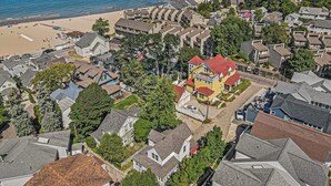 An aerial view of a coastal residential area with houses, a beach, and a large yellow building with a red roof.