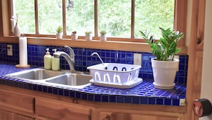 Una cocina con salpicadero de azulejos azules, armarios de madera, un lavamanos doble y una ventana con vista a follaje.