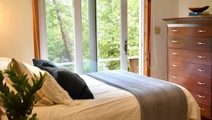 Un dormitorio con cama, cómoda, planta en maceta y vista a la vegetación exterior.