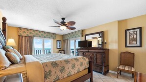Une chambre d’hôtel avec un grand lit, une commode en bois, une chaise, un ventilateur de plafond et un balcon avec vue.