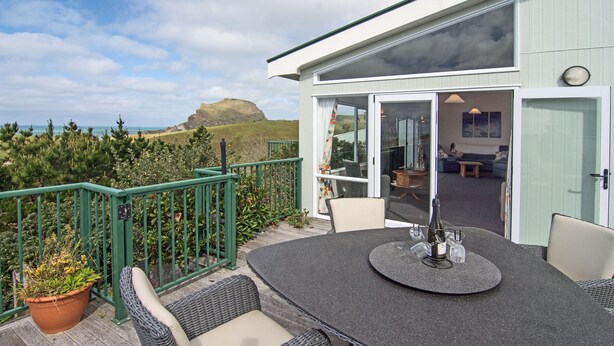 A deck with wicker furniture and a table, overlooking a scenic landscape. - Castlepoint - Private family beach home with stunning views capturing the sun. (Castlepoint)