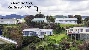 A residential area with houses on a hillside, including a house with a balcony and a satellite dish. - Castlepoint - Private family beach home with stunning views capturing the sun. (Castlepoint)