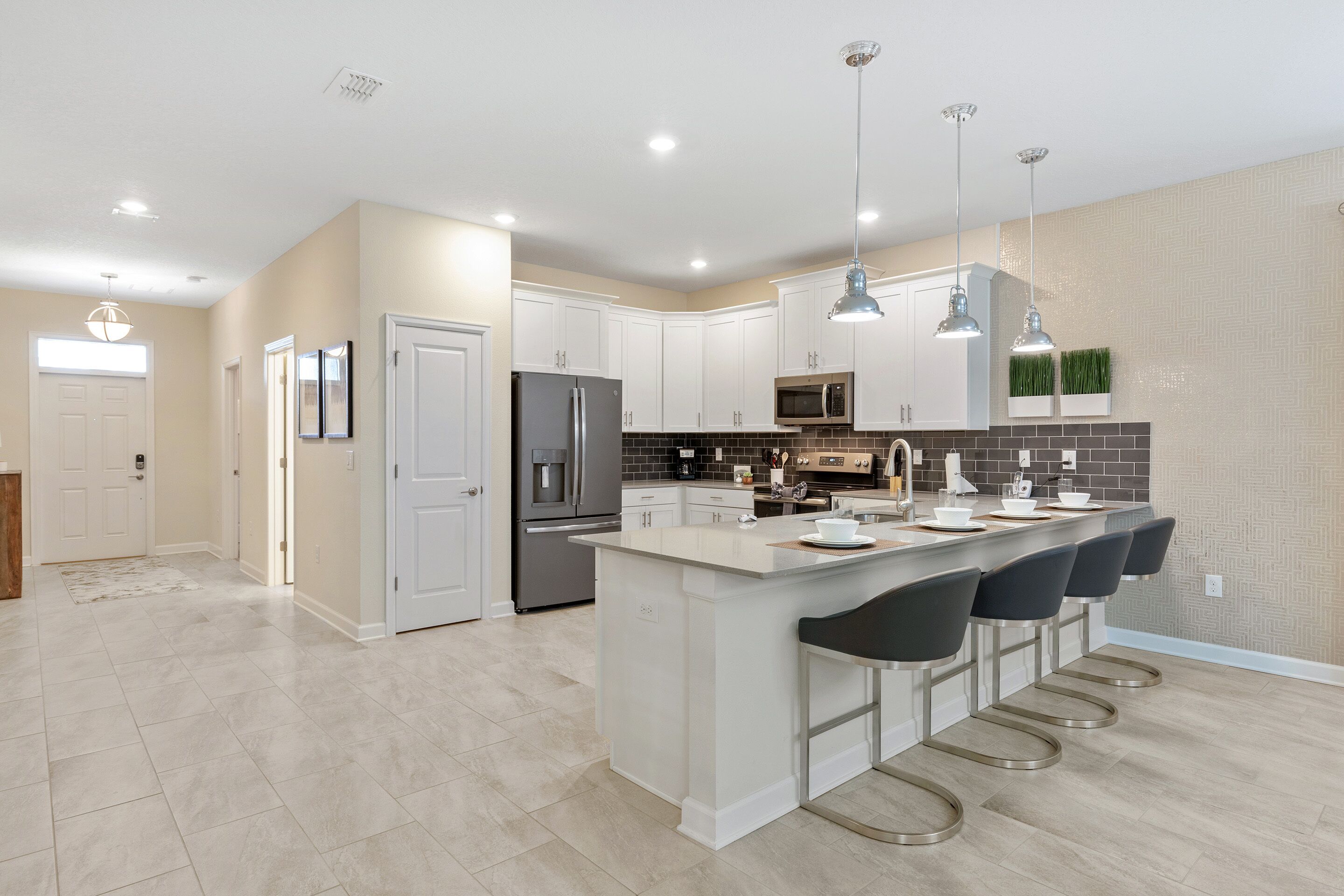 A modern kitchen with white cabinetry, a central island with bar stools, stainless steel appliances, and pendant lighting.