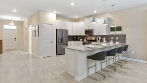 A modern kitchen with white cabinetry, a central island with bar stools, stainless steel appliances, and pendant lighting.