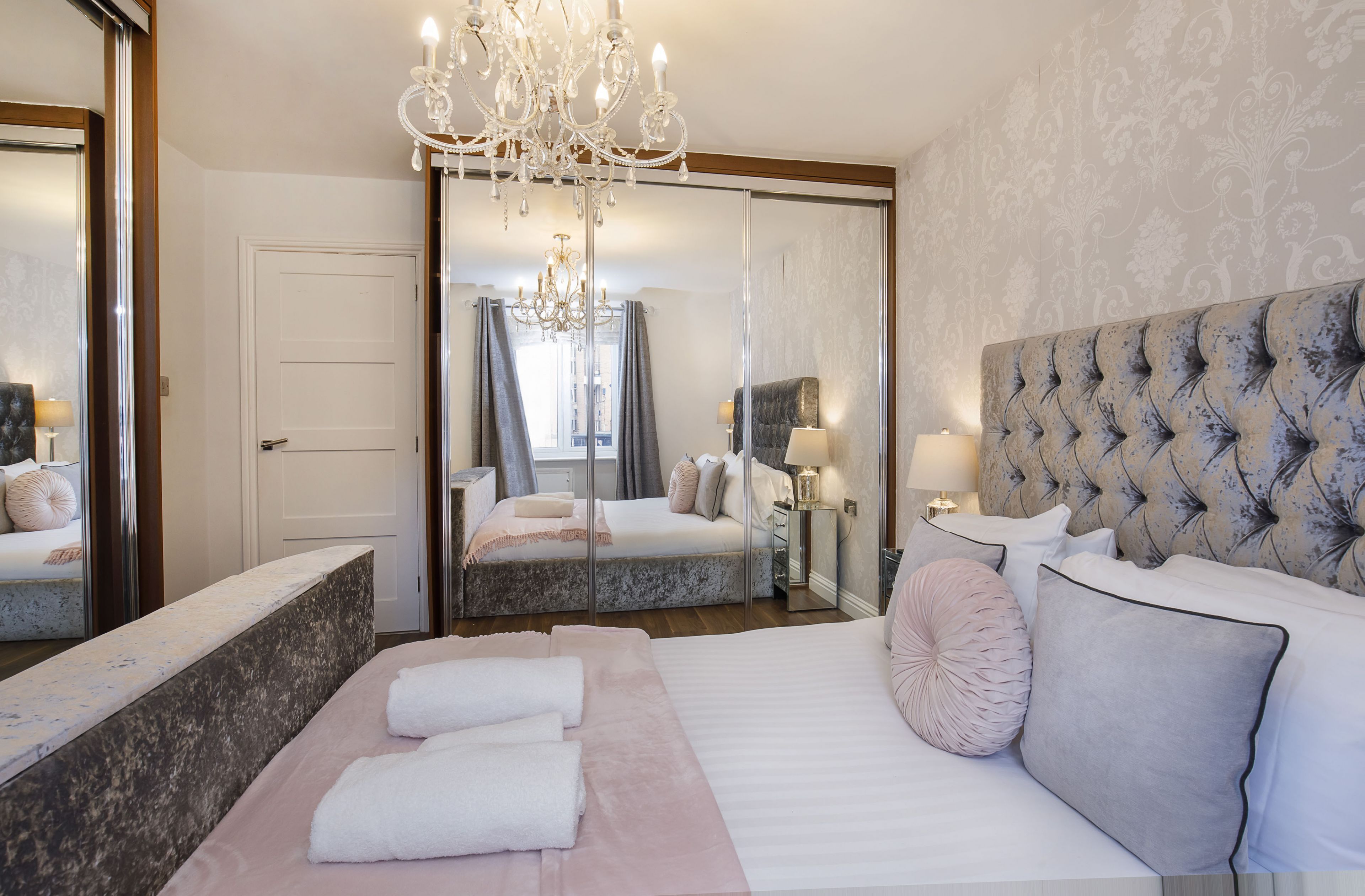 A bedroom with a large bed, a chandelier, a mirror, and a wardrobe.
