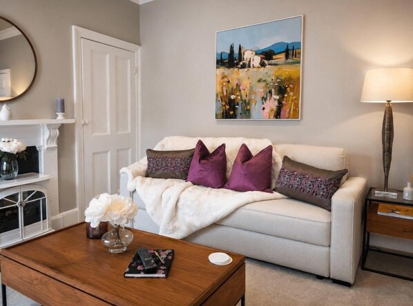 A living room with a white sofa, a coffee table with a vase of flowers, a painting on the wall, and a lamp on a side table.