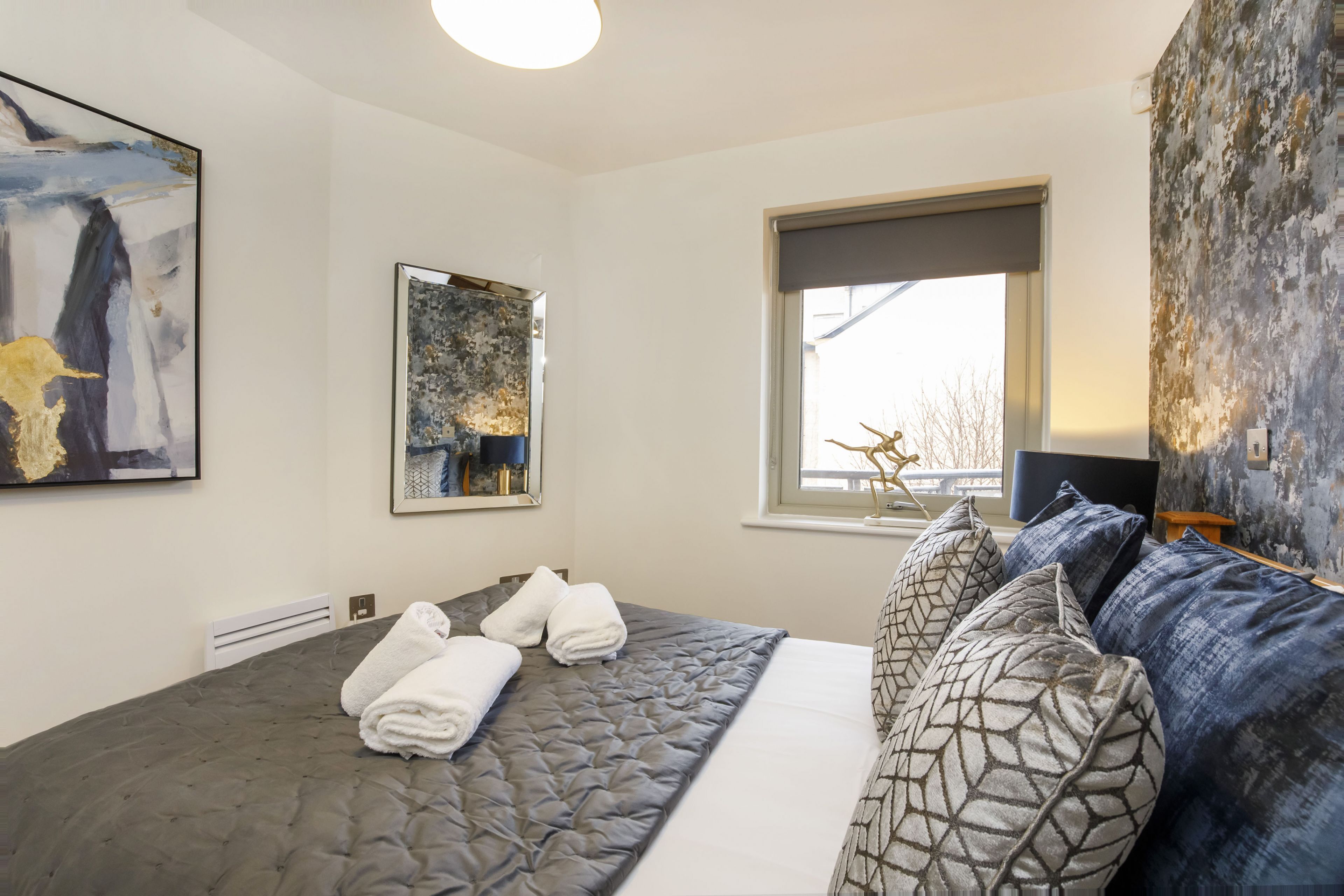 Ein Hotelzimmer mit einem großen Bett, zwei Gemälden, einem Fenster mit Ausblick und einer strukturierten Wand.