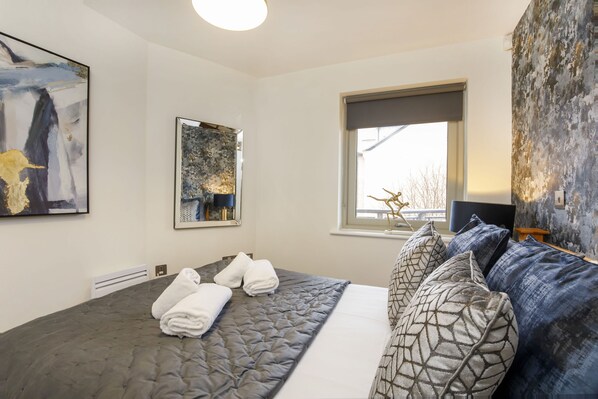 A hotel room with a large bed, two paintings, a window with a view, and a textured wall. - Dixons Yard City centre Apartment (York)