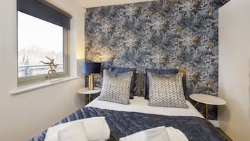 Un dormitorio con cama, dos mesitas de noche, lámpara y ventana con vistas.