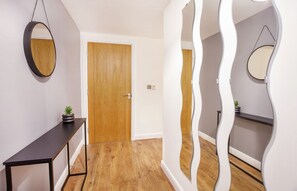 A hallway with a wooden door, a round mirror, and a console table with a potted plant. - Dixons Yard City centre Apartment (York)