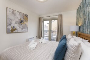 A hotel room with a bed, a window, a painting, and a lamp.