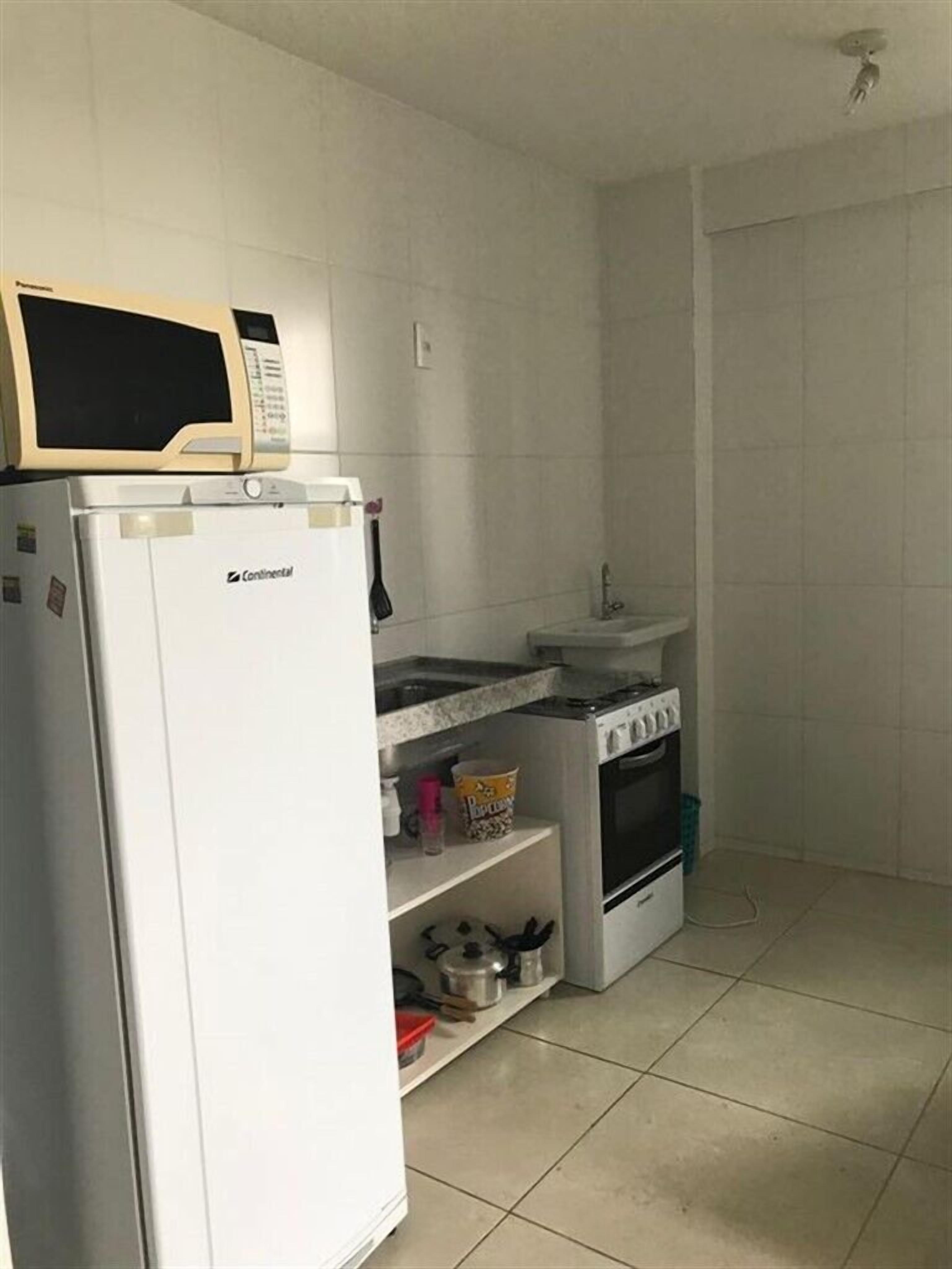 Cozinha compacta com eletrodomésticos brancos, incluindo geladeira, micro-ondas, fogão e pia.