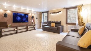 A spacious living area with a large flat-screen TV, a sofa, a bench, and a window with curtains.
