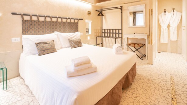 A hotel room with a large bed, a wooden headboard, a mirror, a vanity with a sink, and two white robes hanging on hooks.
