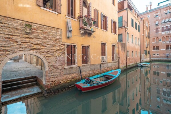 A narrow canal with a row of buildings on one side. A small boat is docked at the canal's edge.