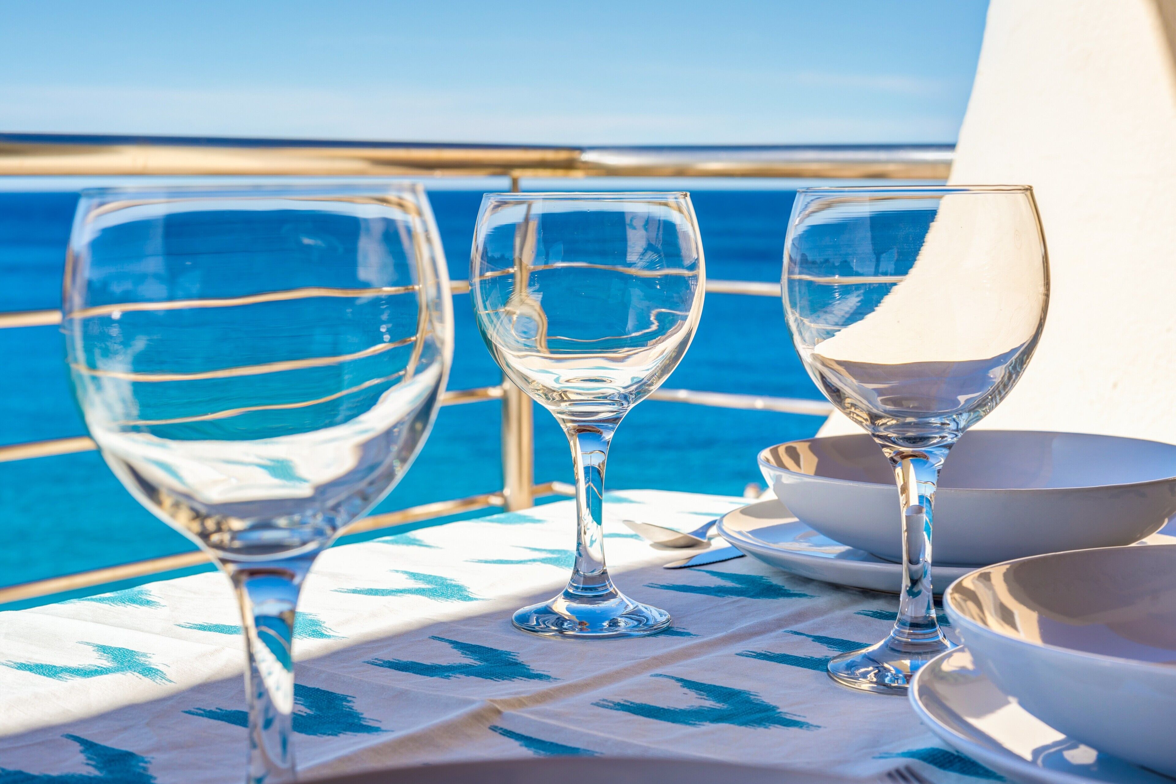 Three wine glasses on a table with a view of the ocean.