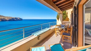 A balcony with a view of the sea, wooden furniture, and a sliding door. - Holiday Apartment "Mirador" with Sea Views and Pool (Cala San Vicens)