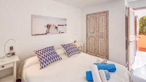 A bedroom with a bed, pillows, a bedside table with a lamp, a wall-mounted artwork, and a wooden wardrobe. - Holiday Apartment "Mirador" with Sea Views and Pool (Cala San Vicens)