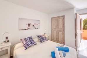 Un dormitorio con cama, almohadas, una mesita de noche con lámpara, una obra de arte en la pared y un armario de madera.