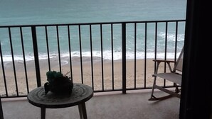 A balcony with a view of the ocean, a small round table with a plant, and a single chair.