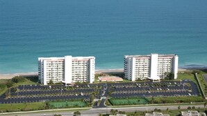 A coastal hotel with two high-rise buildings, a parking lot, and a view of the ocean.