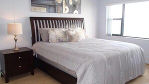 A bedroom with a bed, a nightstand, a lamp, and a window.
