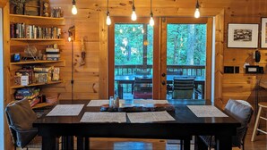 A wooden cabin interior with a dining table, chairs, bookshelves, and a view of the outdoors. - Mountain Cabin on Cooper Creek (Suches)