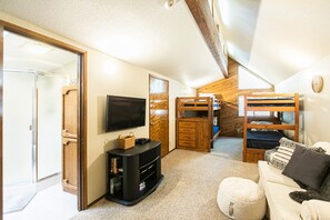 Une chambre mansardée chaleureuse, avec un lit superposé, une télévision, une commode en bois et un canapé confortable.