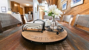 A wooden table with a tray that reads "HAPPINESS IS HOME." There are two metal baskets and a clear vase with white flowers.