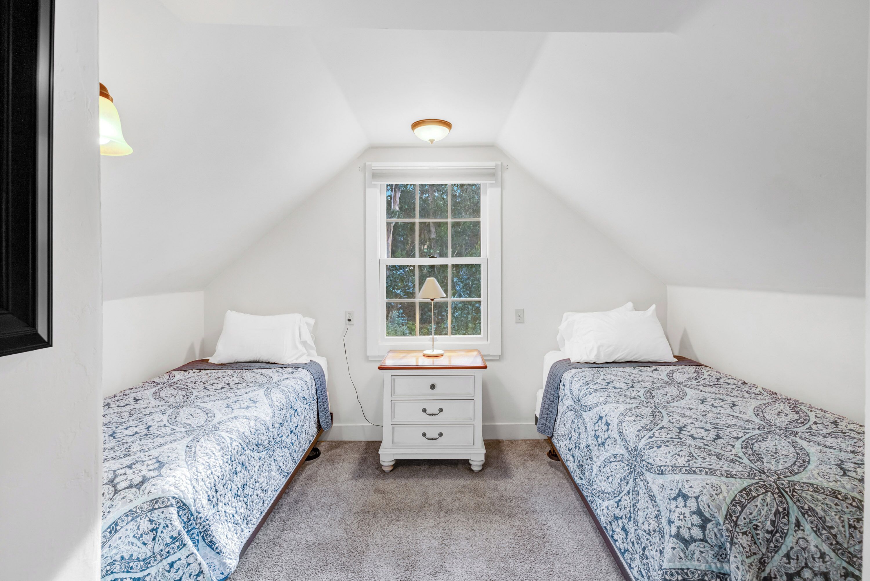 A bedroom with two beds, a window, a nightstand, and a ceiling light.
