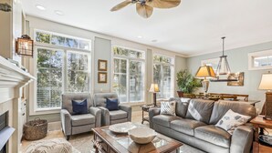 A spacious living room with a fireplace, large windows, a ceiling fan, and a dining area. - 27 Corine Ln, Close to Beach, Free Golf, Pool, Beach Shuttle* (Hilton Head Island)