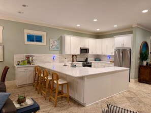 A modern kitchen with white cabinetry, a central island with bar stools, a microwave, and a stainless steel refrigerator.