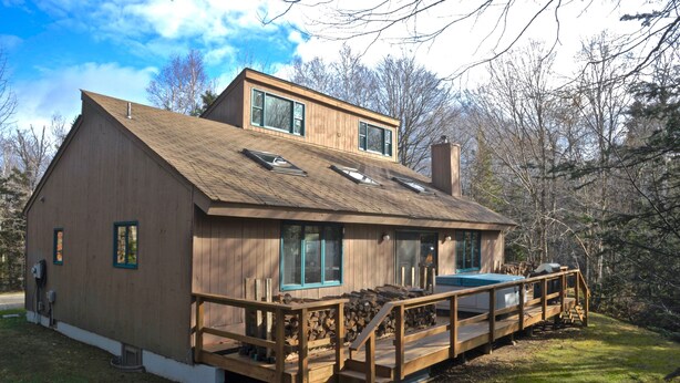 A wooden cabin with a deck, large windows, and a chimney.