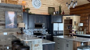 Une cuisine spacieuse avec des meubles de couleur sombre, un îlot central en pierre et un plafond en bois rustique.