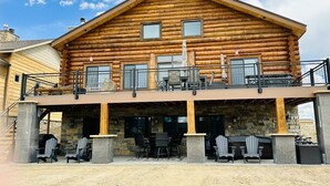 Une cabane en rondins dotée d’un balcon, d’un espace salon extérieur et de murs en pierre.