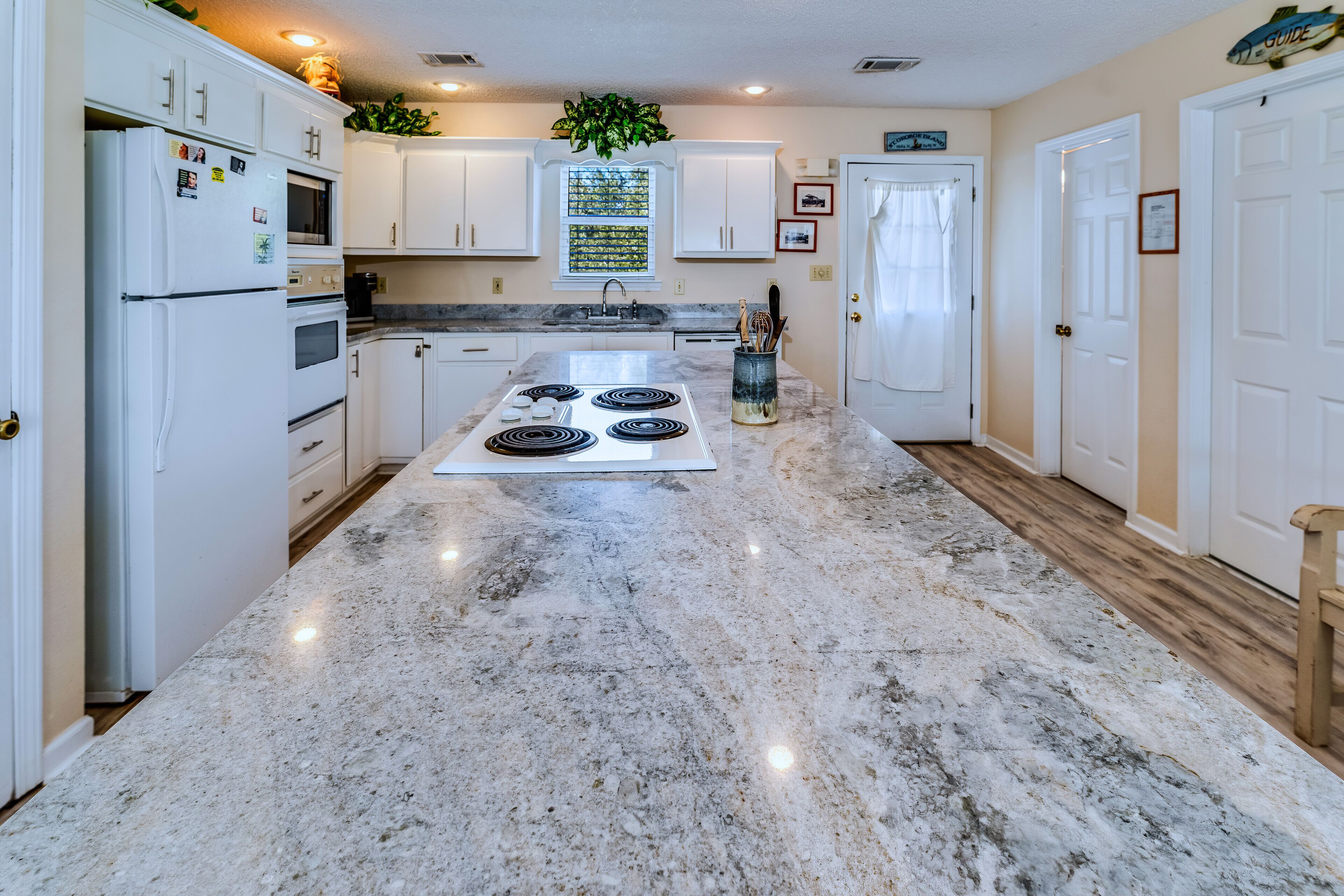 A kitchen with white cabinets, a granite countertop, a built-in oven, and a stainless steel range hood.