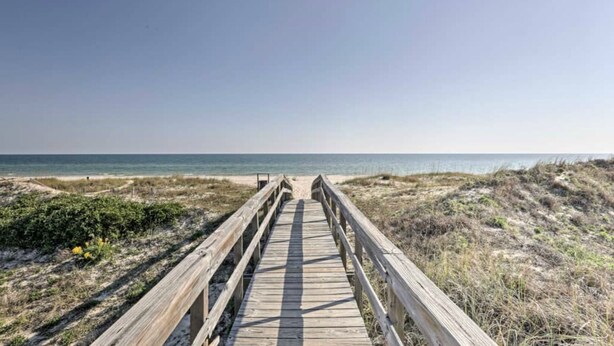 Een houten looppad naar een strand met duinen en schaarse begroeiing.